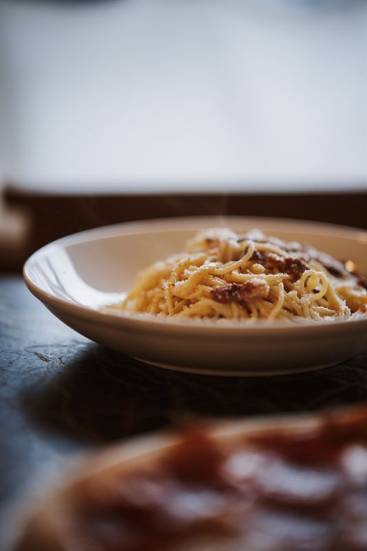 A bowl of spaghetti carbonara with guanciale and grated Parmesan, steam rising