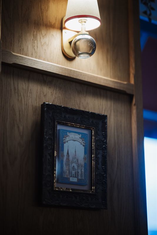 A wall lamp above a framed vintage Milan souvenir print on oak panelling