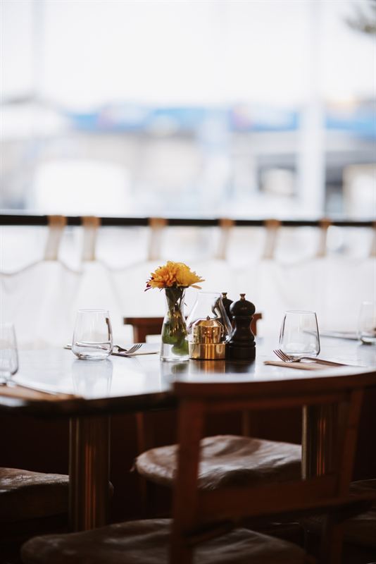 A table by the window at Nucci set with glasses, a small vase of flowers and a brass lamp