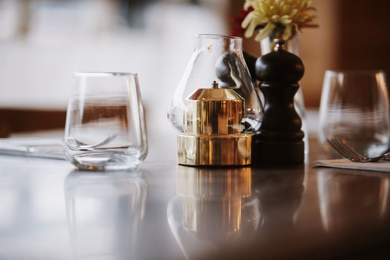 A brass table lamp, pepper mill and glasses on a polished table at Nucci