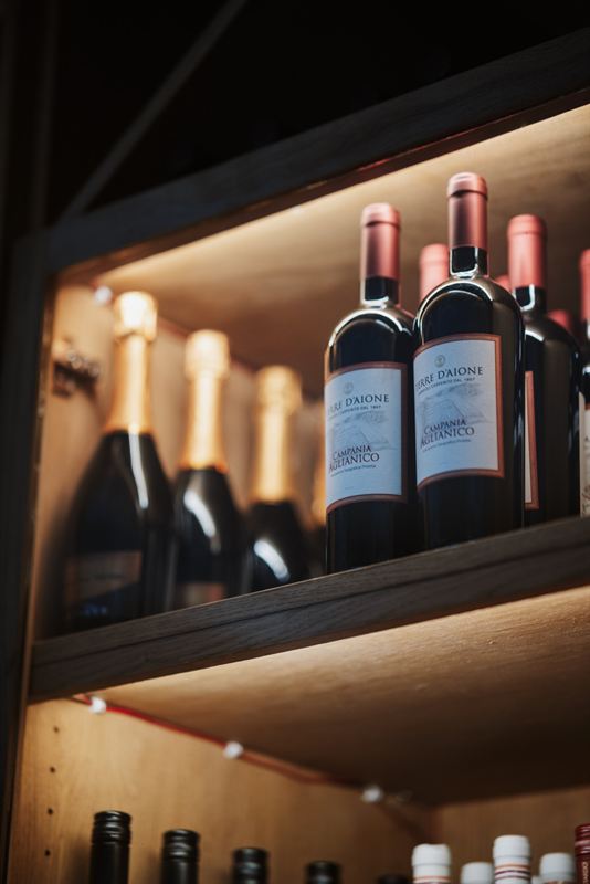 Bottles of Campania Aglianico and sparkling wine on a lit oak shelf